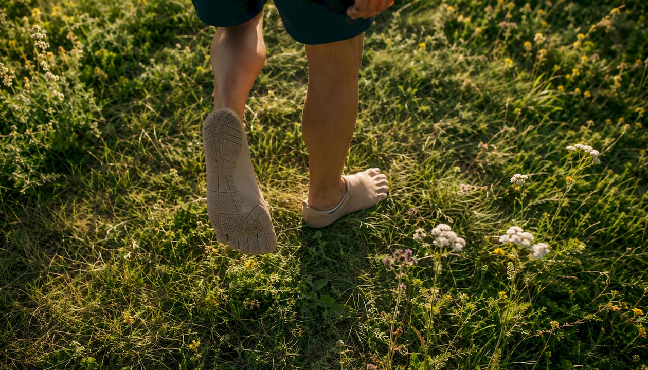 Eine Person läuft mit minimalistischen Barfußschuhen über den Waldboden.